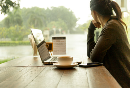 Woman with laptop sitting in restaurant and looking out at the rain